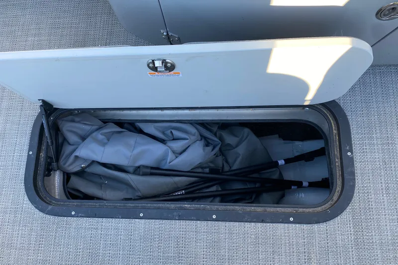 Slide: The Image of Open storage compartment on 2022 Manitou 25 OASIS RF SHP boat with folded cover inside. - 27