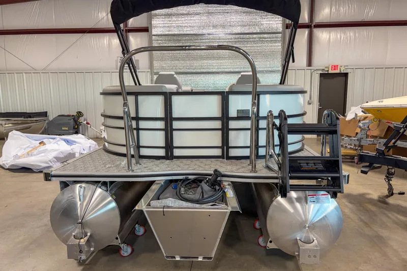 Slide: The Image of 2026 Trifecta 24RF LE pontoon boat in a warehouse, rear view with ladder and railing. - 2