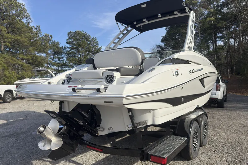 Slide: The Image of 2026 Crownline Eclipse E255 boat on trailer, parked outdoors with trees in background. - 3