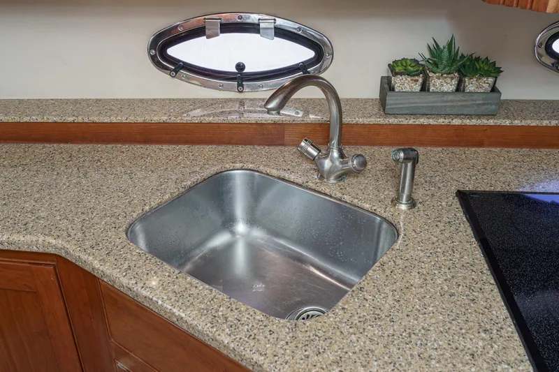Slide: The Image of 2004 Cruisers Yachts 540 Express kitchen sink with granite countertop and porthole window. - 31