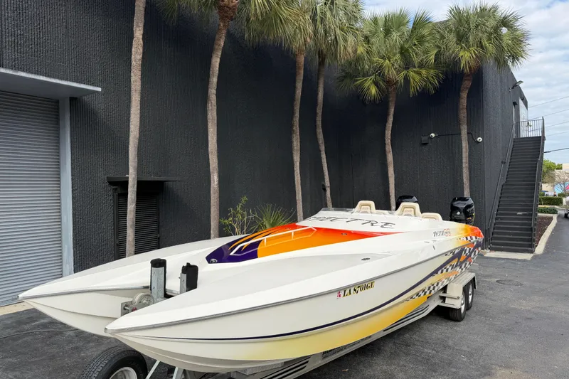 Slide: The Image of 2000 Spectre 30 Cat powerboat with vibrant graphics, parked near palm trees and a black building. - 1