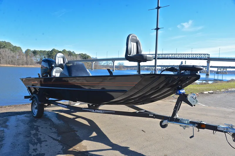 Slide: The Image of 2021 Lowe Legacy boat on trailer by a lake with bridge in background. - 14