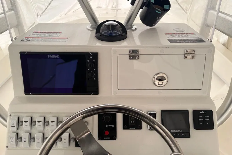 Slide: The Image of Control panel of a 2025 Dusky 227 boat featuring Simrad electronics and Suzuki controls. - 2