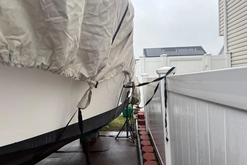 Slide: The Image of Covered 2025 Dusky 227 boat secured beside a white fence on a rainy day. - 9
