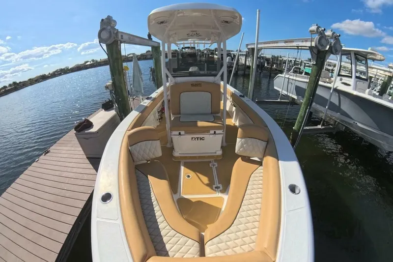 Slide: The Image of 2020 Velocity 262cc boat docked, featuring tan seating and spacious deck under clear blue sky. - 11