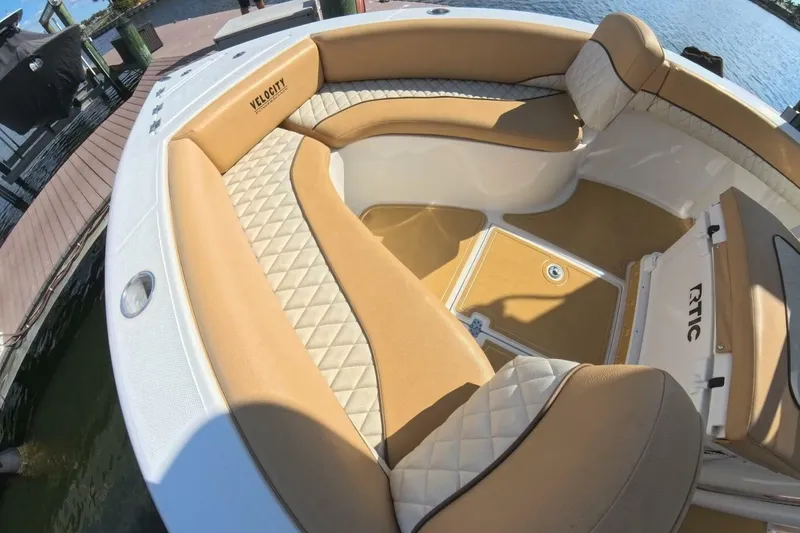Slide: The Image of 2020 Velocity 262cc boat interior with tan and white seating, docked by the water. - 12