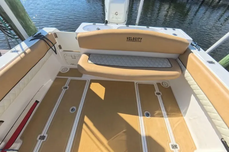 Slide: The Image of 2020 Velocity 262cc boat interior with tan seating and deck, docked by water. - 15