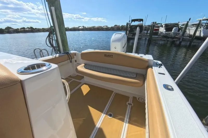 Slide: The Image of 2020 Velocity 262cc boat interior with tan seating, docked by a serene waterfront. - 17