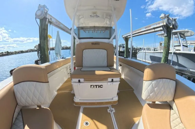 Slide: The Image of 2020 Velocity 262cc boat interior with tan and white seating, docked by the water. - 2