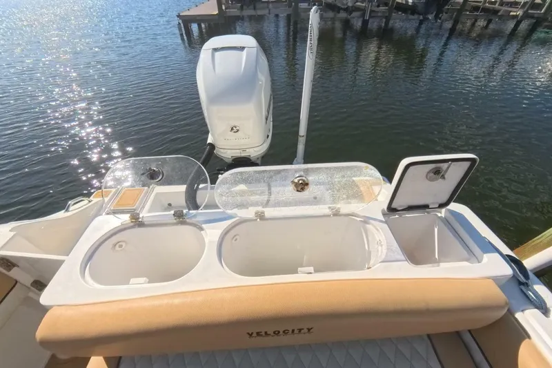 Slide: The Image of 2020 Velocity 262cc boat with open storage compartments and outboard motor on a sunny day. - 20