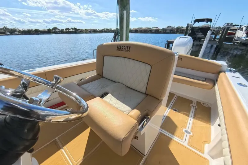 Slide: The Image of 2020 Velocity 262cc boat interior with tan seating and steering wheel, docked by the water. - 5