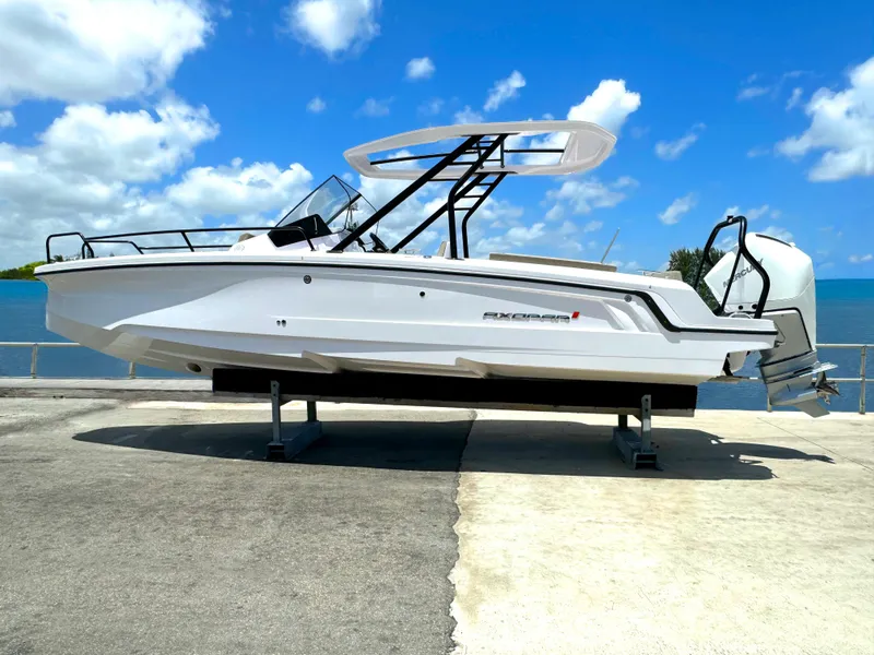The Image of 2024 Axopar 25 Cross Top boat on display by the water under a clear blue sky. - 1