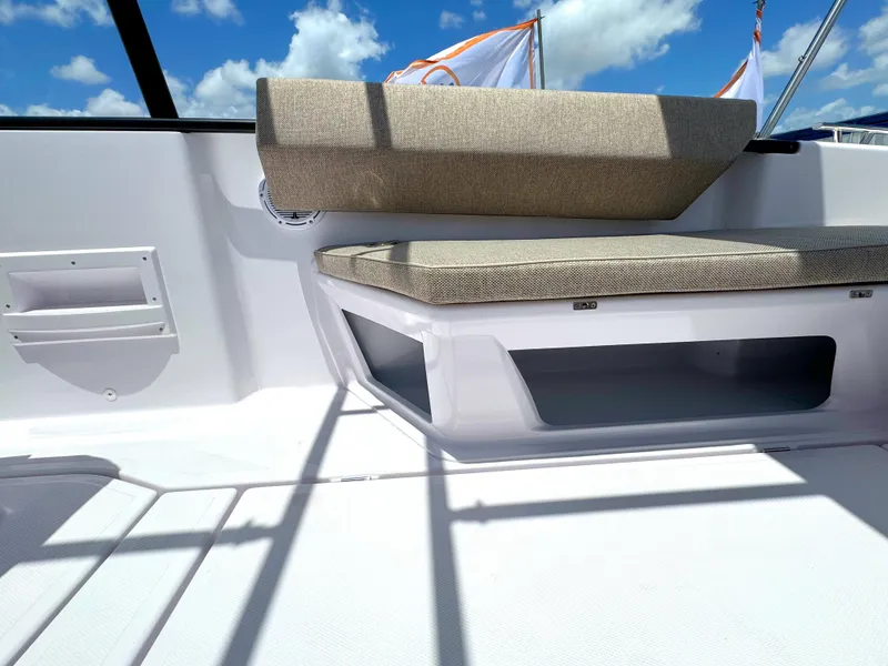 Slide: The Image of 2024 Axopar 25 Cross Top boat interior with cushioned seating and storage, under a clear blue sky. - 6