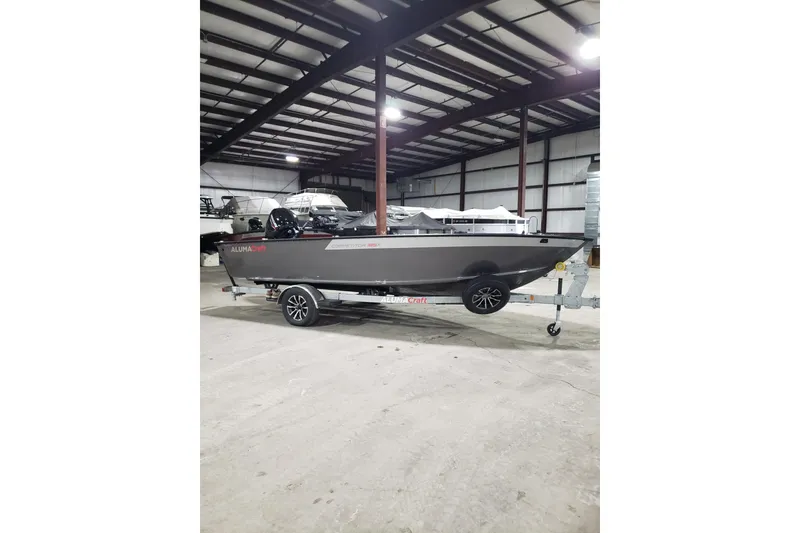 Slide: The Image of 2026 Alumacraft Competitor 185X Tiller boat on trailer in warehouse setting. - 18