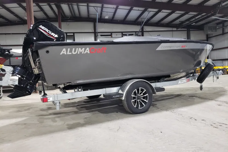 Slide: The Image of 2026 Alumacraft Competitor 185X Tiller boat on trailer in warehouse setting. - 2