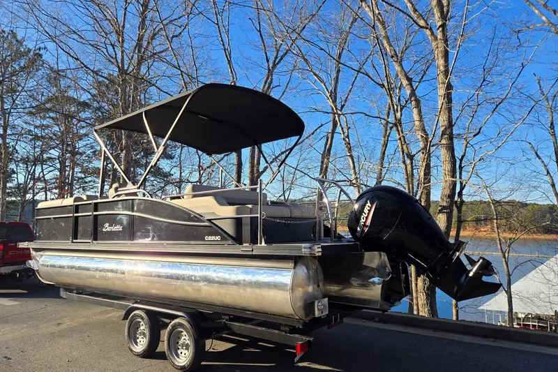 Slide: The Image of 2020 Barletta C22UC pontoon boat on trailer by a lake, under clear blue sky. - 3
