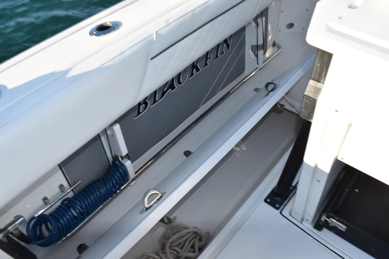 Slide: The Image of 2022 Blackfin 272 CC boat interior with storage compartment and coiled blue hose. - 25