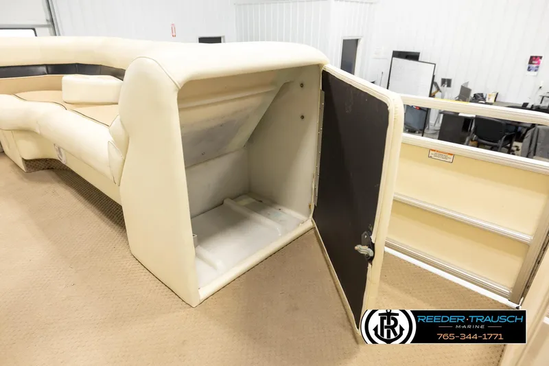 Slide: The Image of 2004 AquaPatio 220 RE boat interior with open storage compartment, beige seating, and carpeted floor. - 23