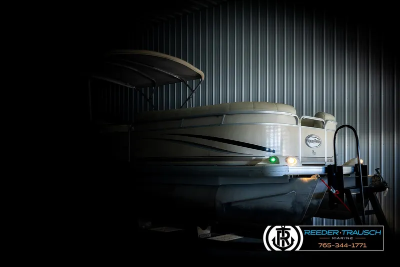 Slide: The Image of 2004 AquaPatio 220 RE pontoon boat in storage, partially illuminated, with Reeder-Trausch Marine logo. - 4