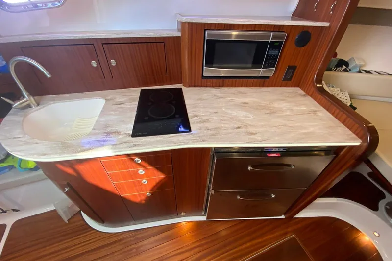 Slide: The Image of 2018 Pursuit OS 385 Offshore yacht kitchen with sink, stove, microwave, and wooden cabinetry. - 12