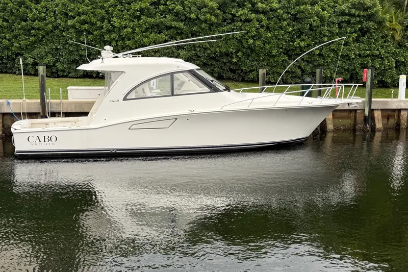 The Image of 2012 Cabo 40 Hardtop Express yacht docked by lush greenery. - 1