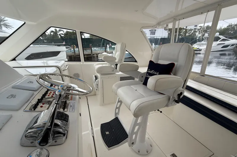 Slide: The Image of 2012 Cabo 40 Hardtop Express helm with white seating and steering wheel, docked near yachts. - 3
