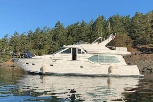 The Image of 2002 Bayliner 5788 yacht with Electronic Cummins QSMs on calm water near forested shore. - 0
