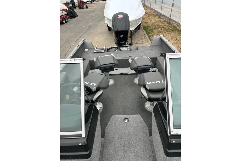 Slide: The Image of 2018 Lund 1775 Impact Sport boat interior with seating and motor, parked outdoors. - 12