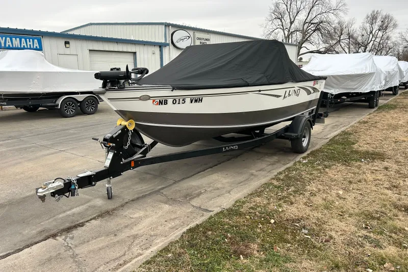 Slide: The Image of 2018 Lund 1775 Impact Sport boat covered, parked on a trailer near a dealership. - 7