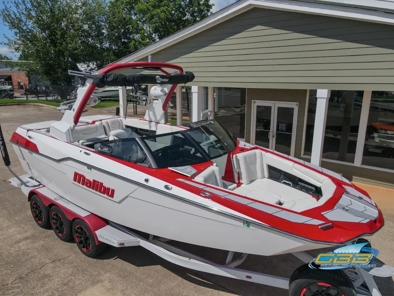 Slide: The Image of 2021 Malibu M240 boat on trailer, red and white design, parked outdoors. - 1