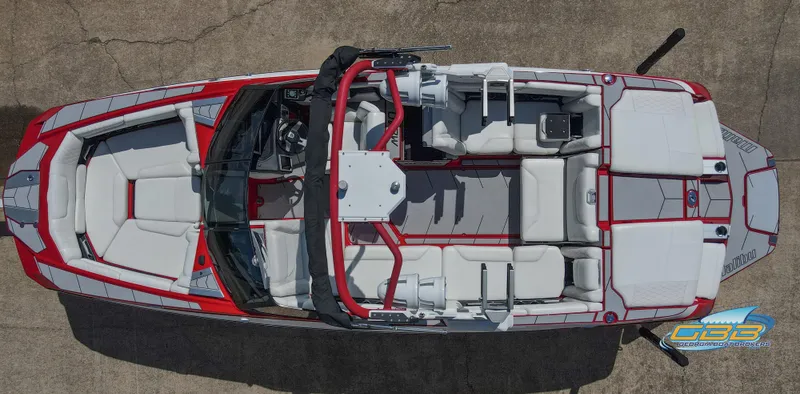 Slide: The Image of 2021 Malibu M240 boat with red and white design, parked on a trailer outside a building. - 2