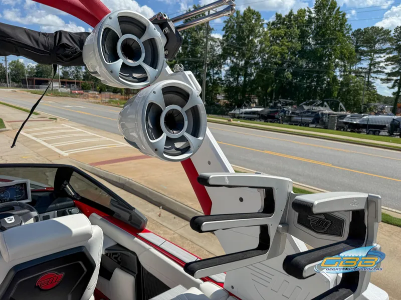 Slide: The Image of 2021 Malibu M240 boat with speakers and wakeboard rack, parked near a road. - 29