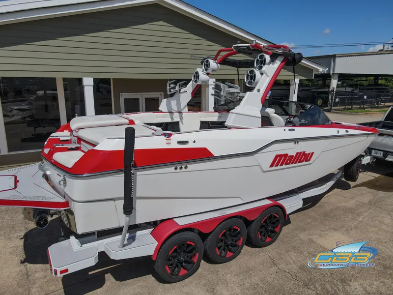 Slide: The Image of 2021 Malibu M240 boat with red accents on a trailer, parked outside a building. - 8