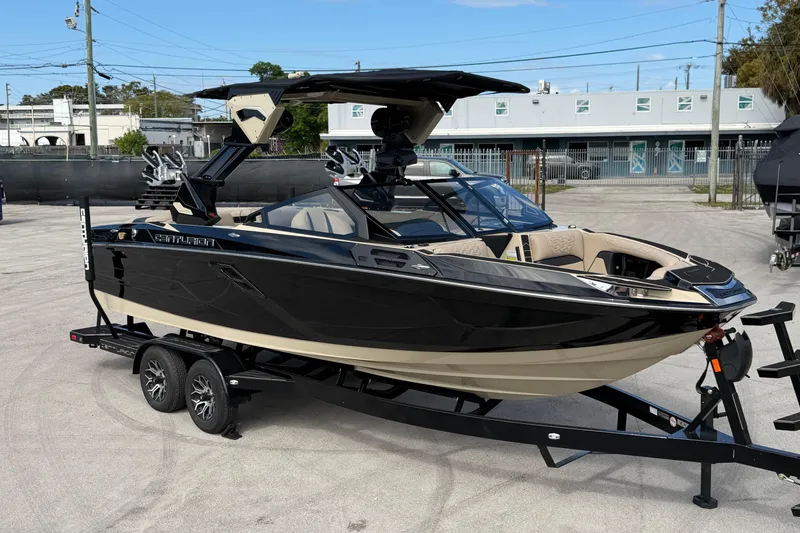 The Image of 2026 Centurion Ri230 boat on trailer, black and beige design, parked outdoors. - 0