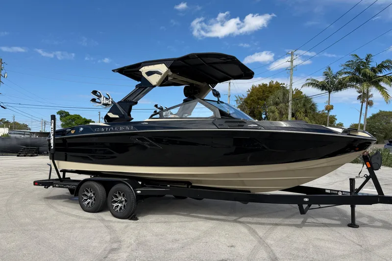 Slide: The Image of 2026 Centurion Ri230 boat on trailer, black and beige, parked outdoors under blue sky. - 11