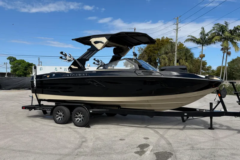Slide: The Image of 2026 Centurion Ri230 boat on trailer, black and beige, parked outdoors. - 2