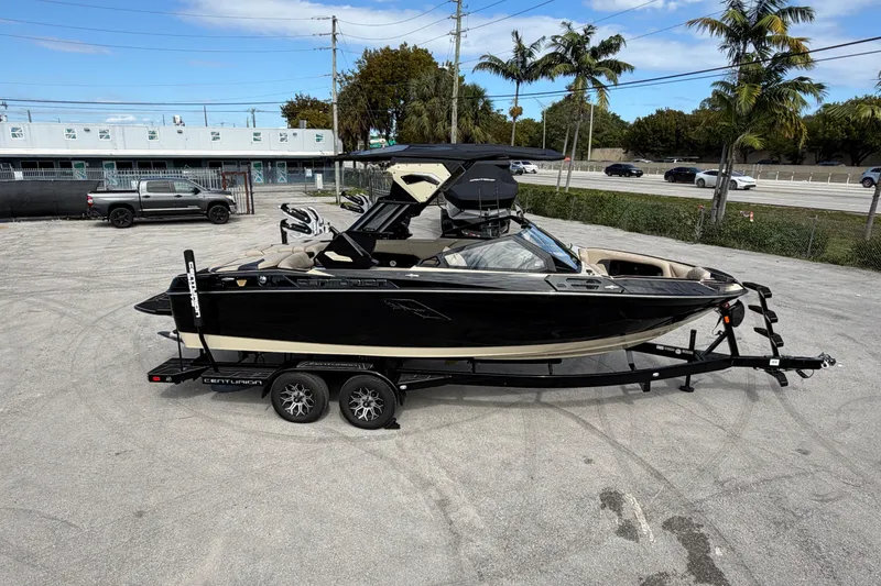 Slide: The Image of 2026 Centurion Ri230 boat on trailer, parked outdoors with palm trees and vehicles nearby. - 9
