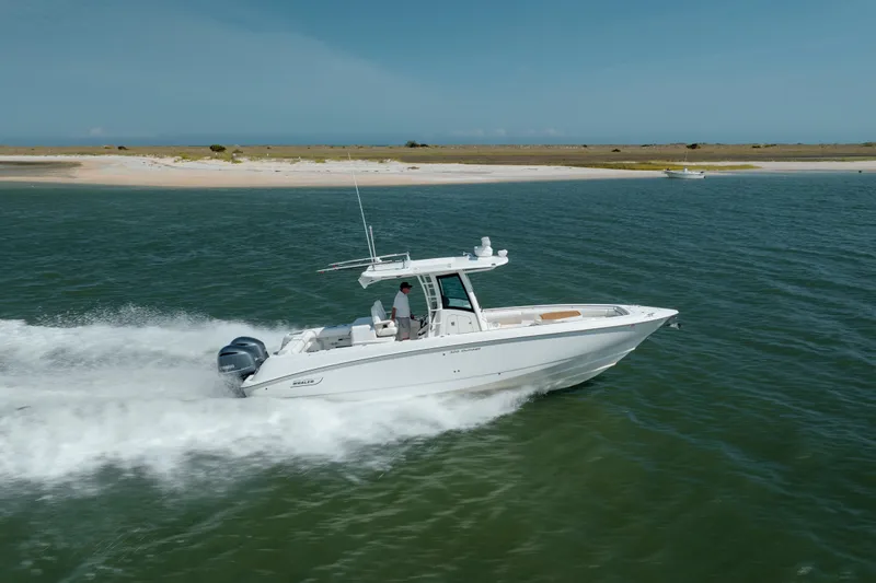 The Image of 2013 Boston Whaler 320 Outrage cruising on open water near a sandy shoreline. - 0