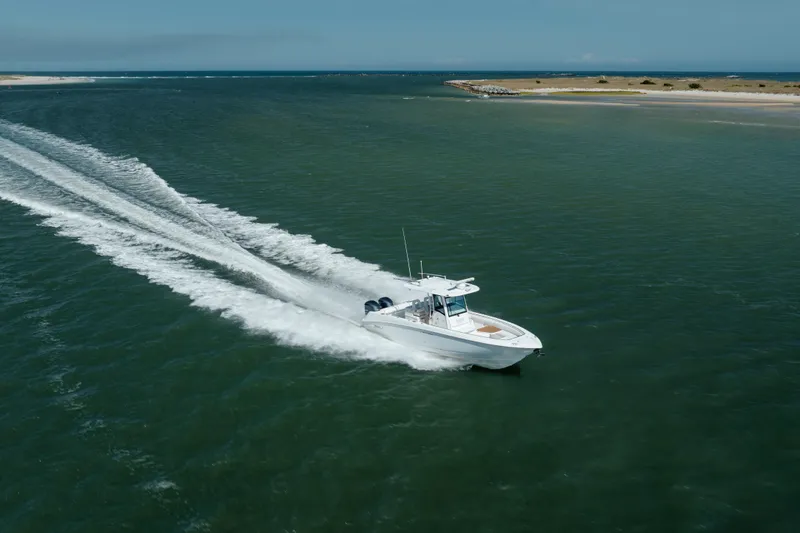 Slide: The Image of 2013 Boston Whaler 320 Outrage cruising on open water near a sandy shoreline. - 2