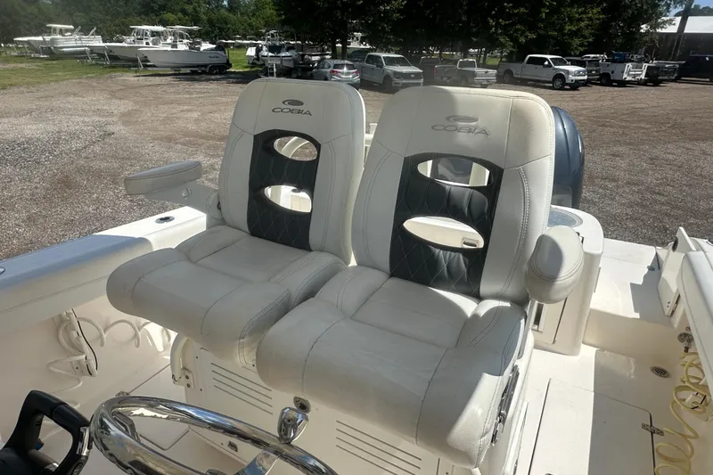 Slide: The Image of 2023 Cobia 262 Center Console boat seats with steering wheel, parked outdoors. - 15