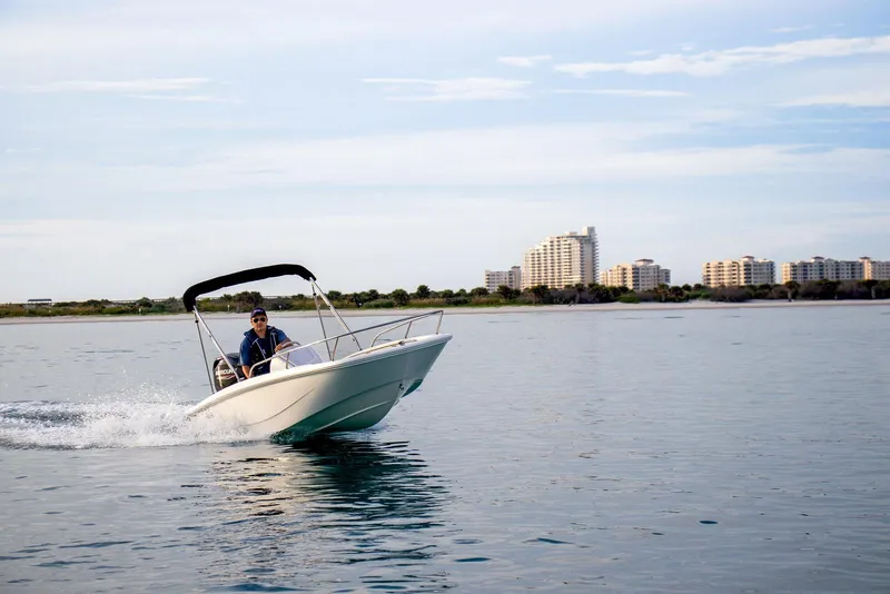 Slide: The Image of 2026 Boston Whaler 130 Super Sport cruising on calm waters near coastal buildings. - 10