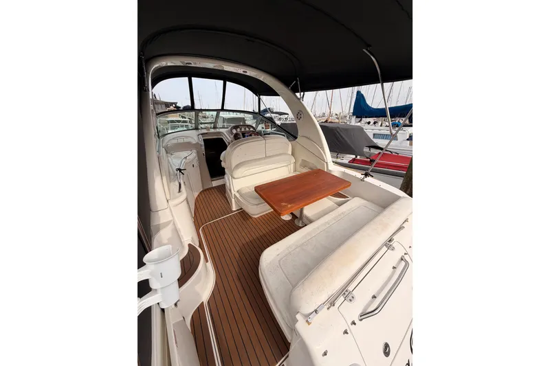 Slide: The Image of 2005 Sea Ray 300 Sundancer interior with seating and wooden table in marina setting. - 11