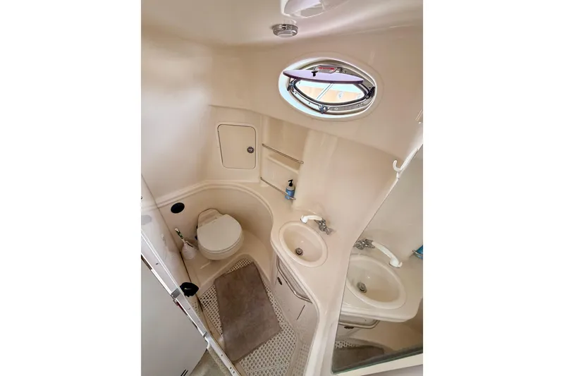 Slide: The Image of Compact bathroom in 2005 Sea Ray 300 Sundancer boat, featuring toilet, sink, and porthole window. - 27