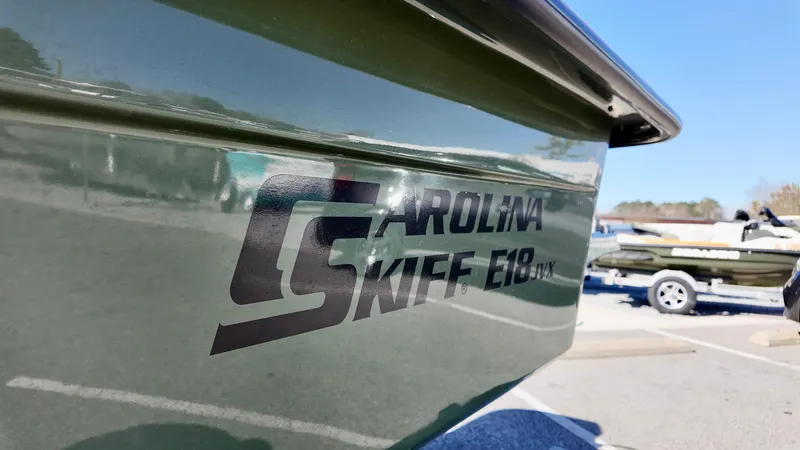 Slide: The Image of 2025 Carolina Skiff E18 JVX CC boat, green hull, parked on trailer. - 2