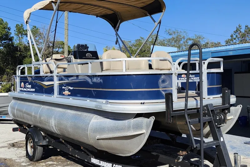 The Image of 2023 Sun Tracker Bass Buggy 18 DLX pontoon boat on trailer, blue and beige design. - 1