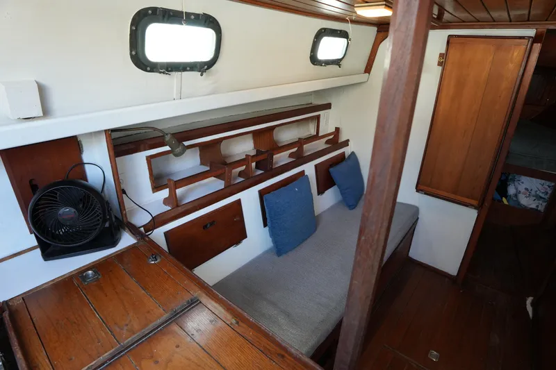 Slide: The Image of 1975 Westsail 32 interior with wooden furnishings, blue cushions, and a small fan. - 16