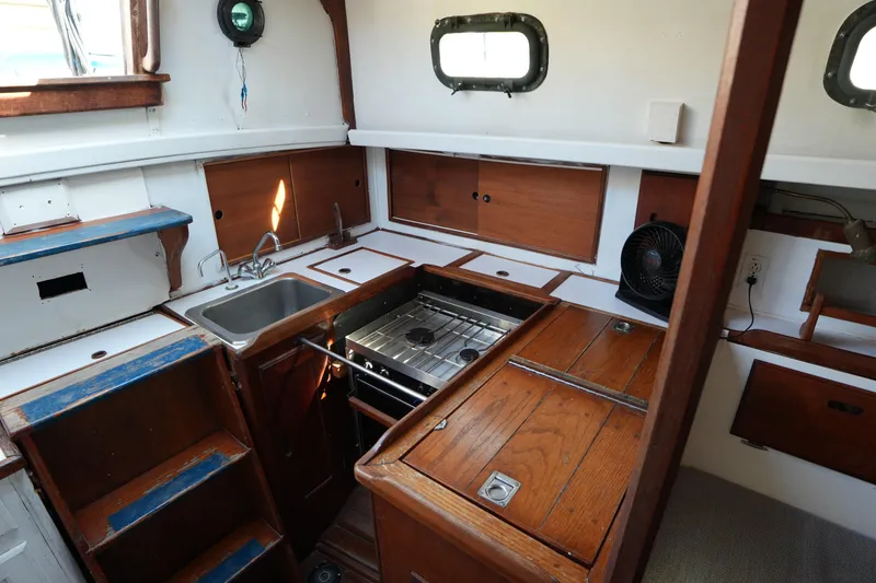 Slide: The Image of 1975 Westsail 32 sailboat interior kitchen with wooden cabinetry and compact stove. - 17
