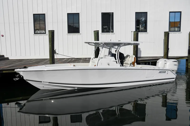 The Image of 2026 Jupiter 30 boat docked by a white building, reflecting on calm water. - 0