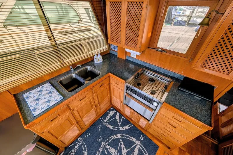 Slide: The Image of 1987 DeFever Trawler kitchen with wooden cabinets, dual sink, stove, and nautical-themed decor. - 12