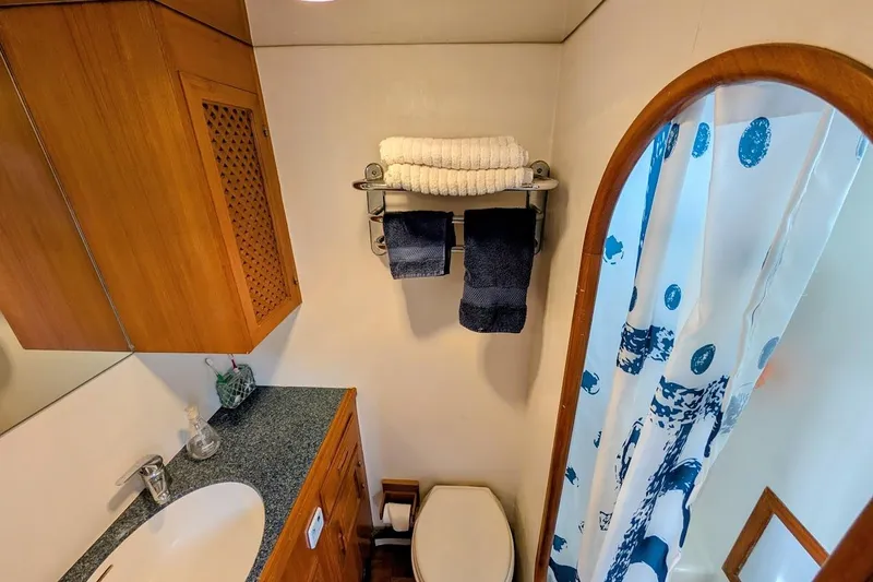 Slide: The Image of 1987 DeFever Trawler bathroom with wooden cabinetry, sink, and nautical-themed shower curtain. - 19